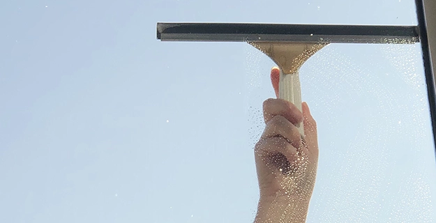 View of a hand with a squeegee cleaning a window.