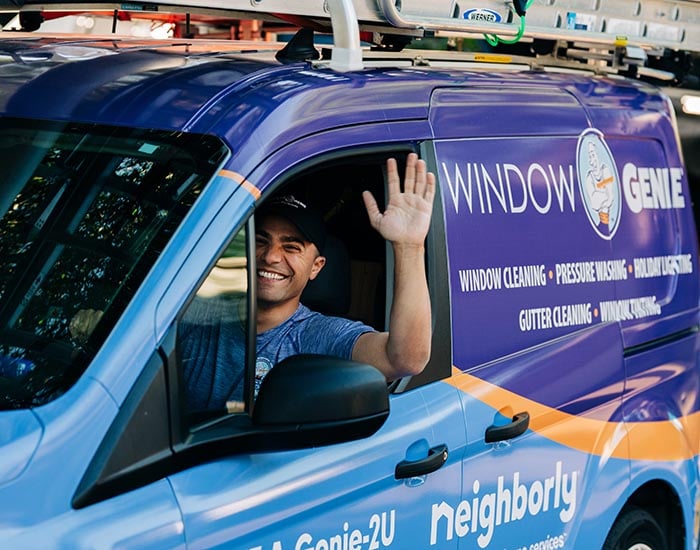 Window Genie tech waving while driving company van to a commercial window cleaning job 