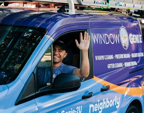 Window Genie tech waving while driving company van to a commercial window cleaning job.