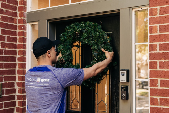 Window Genie professional hanging a holiday wreath on the front door of a house.