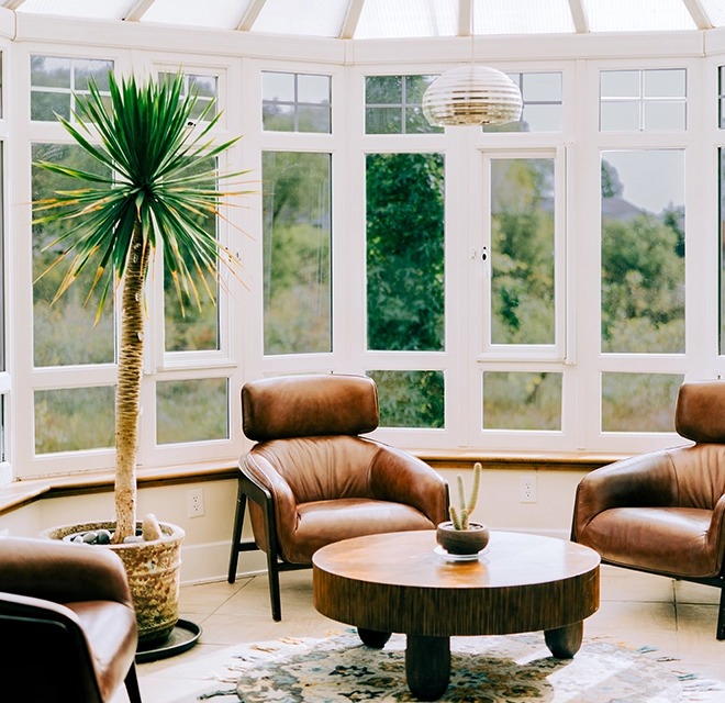 Room surrounded by windows with brown leather chairs.