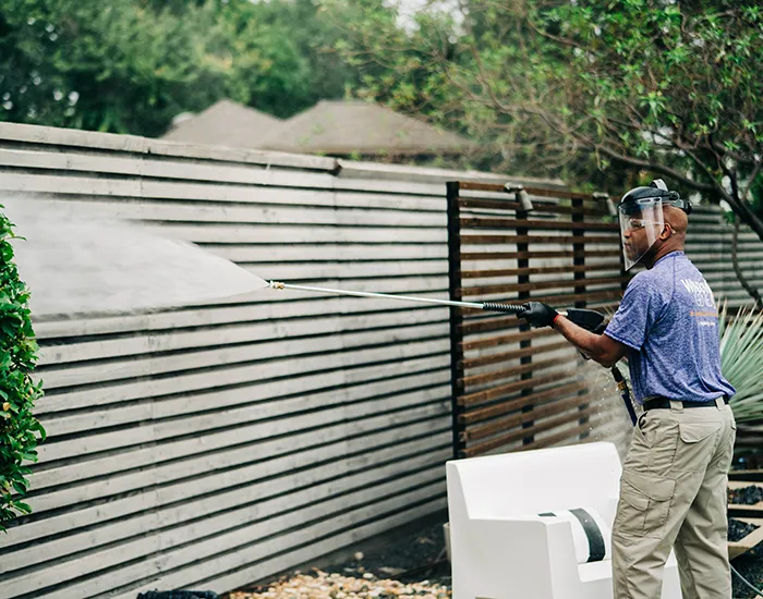 Window Genie tech pressure washing a wood fence at a commercial property.